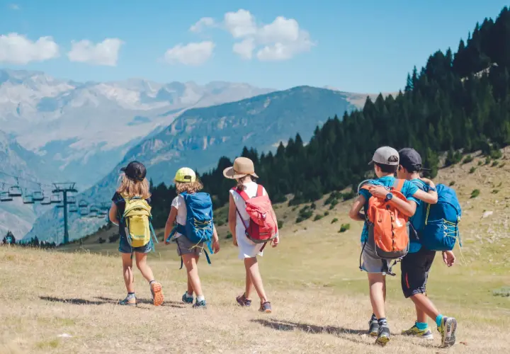 Niños explorando los Pirineos con mochilas, disfrutando de un día soleado con vistas a las montañas y un telesilla.