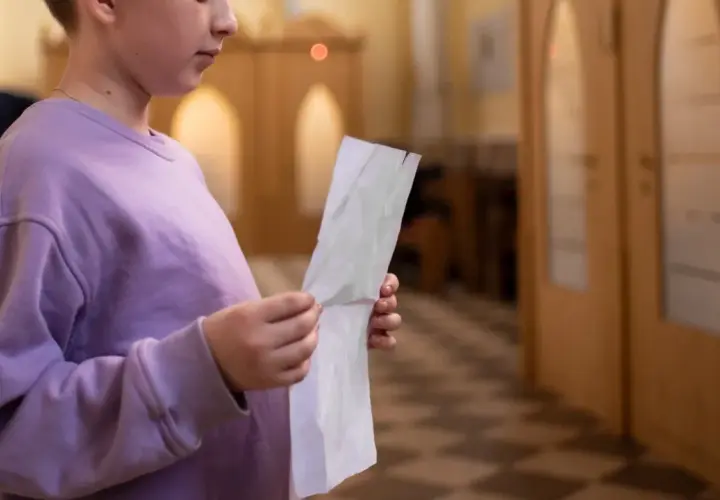 Młoda osoba w fioletowej bluzie trzyma kartkę, przygotowując się do spowiedzi świętej w kościele.