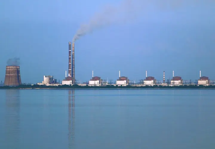 Zaporoże: potężna elektrownia atomowa z chłodnią kominową i dymiącymi kominami, na tle spokojnej wody.