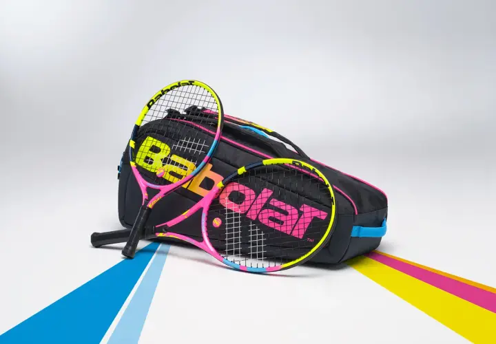 Dwie kolorowe rakiety tenisowe, jakich używałby Rafael Nadal, leżą obok czarnej torby z logo Babolat.