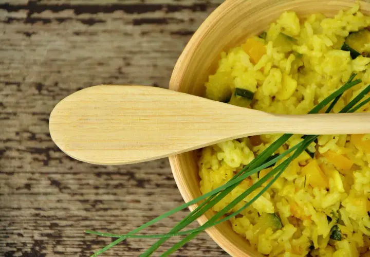Un cucchiaio di legno su un piatto di risotto allo zafferano con zucchine e erba cipollina.