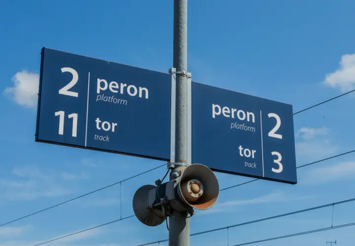 Niebieskie tablice informacyjne na słupie wskazują numery linii kolejowych: peron 2, tor 11 oraz peron 2, tor 3.