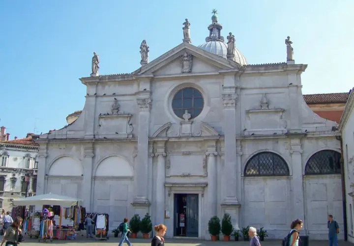 Façade de Santa Maria Formosa à Venise, avec des statues, un dôme et une place animée.