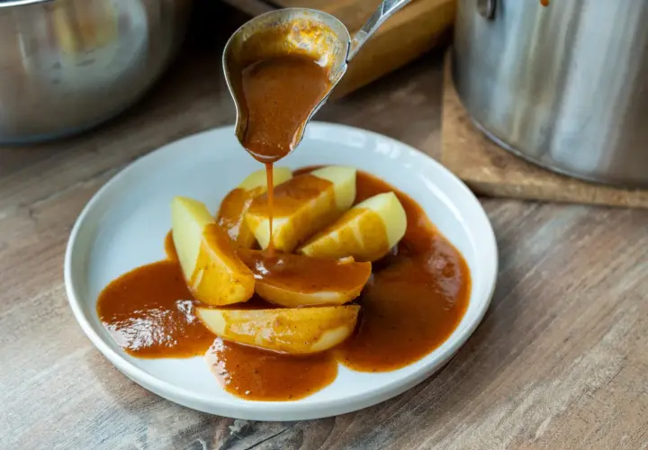 Eine Schöpfkelle gießt eine köstliche braune Sauce über Kartoffelspalten auf einem Teller.