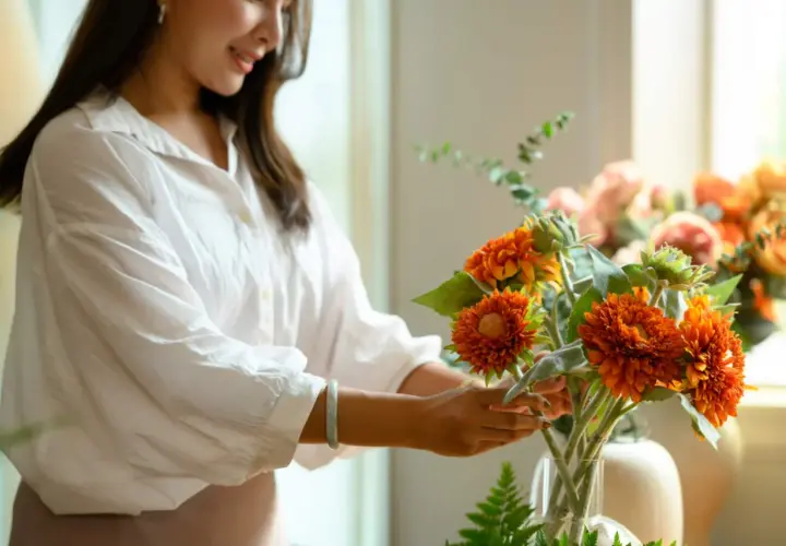 Une femme arrange une composition florale aux couleurs vives, mêlant feuillage et fleurs orangées.