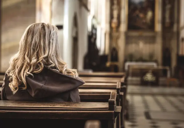 Kobieta z blond włosami siedzi w kościele, odwrócona tyłem. Obraz ilustruje badanie CBOS praktyki religijne.