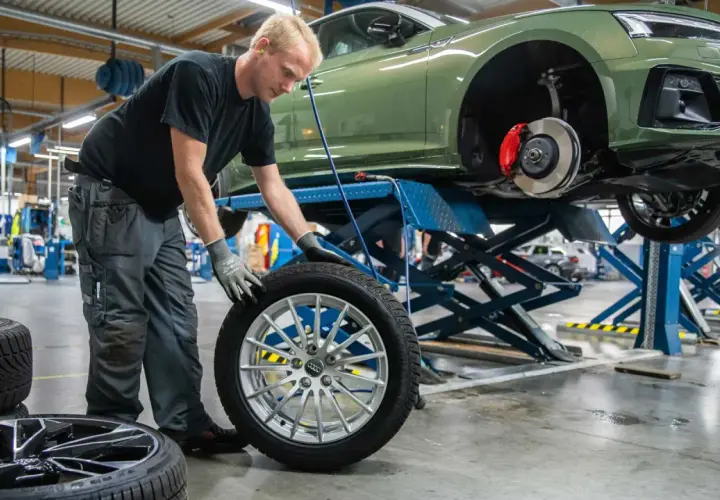 Mekaniker byter däck på en grön Audi. Det är dags för hjulskifte datum, så bilen lyfts upp på en billyft.