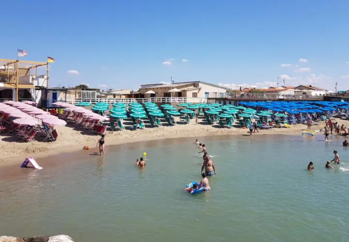 Plage de Marina di Pisa animée, avec des rangées de parasols et de chaises longues sur le sable, et des baigneurs profitant de l'eau claire sous un ciel bleu.