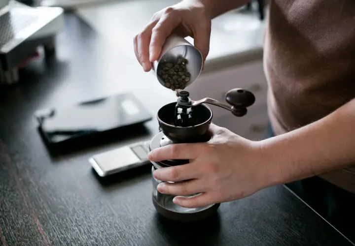 Mani versano chicchi di caffè in un macinino manuale, iniziando la macinazione per un caffè perfetto.