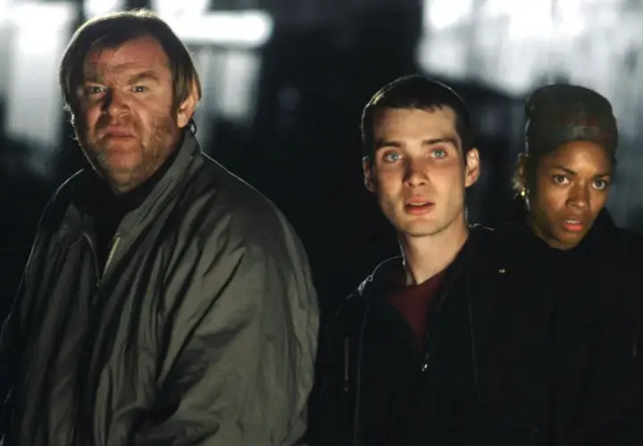 Trzech ocalałych, w tym mężczyzna z groźną miną, przemierzają mroczne ulice w świecie po apokalipsie. To scena z filmu "28 dni później".