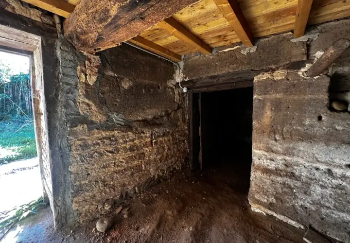 Intérieur d'une maison en pisé en ruine, murs érodés, poutres apparentes. Danger de délabrement.