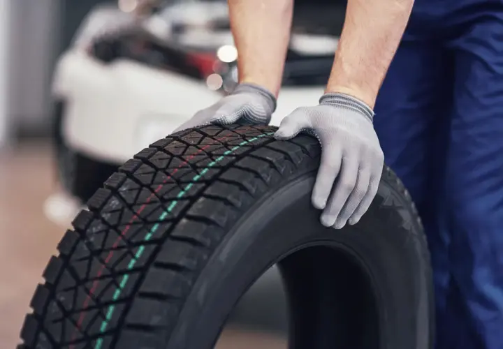 Mechanik w rękawiczkach trzyma oponę zimową. Czy w Polsce jest obowiązek zmiany opon na zimowe? Odpowiedź brzmi: nie.