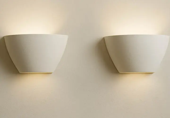 Dos elegantes flexos de pared blancos emiten una luz cálida y difusa, creando un ambiente acogedor en la estancia.