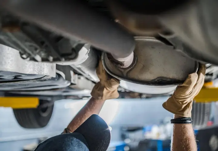 Mani guantate lavorano sul sistema di scarico, forse sostituendo il catalizzatore auto.