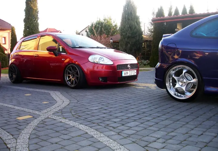 Czerwony Fiat Grande Punto 1.4 z przyciemnianymi szybami i sportowymi felgami, obok niebieski samochód. Rozmiar opon dopasowany do modyfikacji.