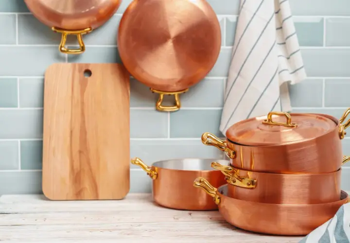 Utensilios de cobre apilados y colgados, junto a una tabla de cortar. Aprende como limpiar cobre para que brillen así.