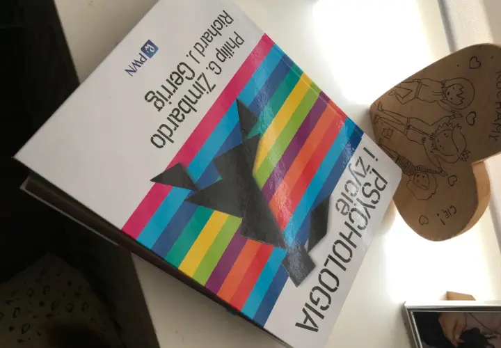 Na biurku leży książka "Psychologia" autorstwa Philipa G. Zimbardo i Richarda J. Gerriga, obok drewniane serce z rysunkami.