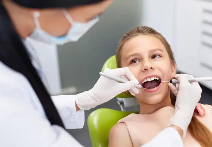 Dziecko u dentysty, które czeka na znieczulenie. Stomatolog w rękawiczkach bada ząb dziewczynki.