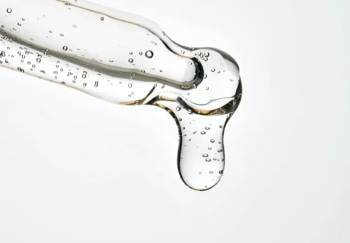 Kropla przejrzystego serum z pęcherzykami powietrza, zawierającego kwasy LHA, spływa z pipety.