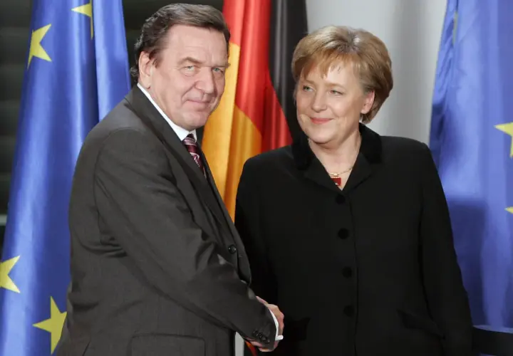 Gerhard Schröder und Angela Merkel, die erste Bundeskanzlerin Deutschlands, vor Flaggen.