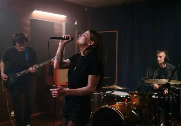 Wokalistka śpiewa do mikrofonu, basista gra na gitarze, a perkusista wybija rytm. Ich wspólna melodia wypełnia studio.