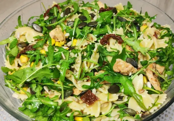 Pyszna sałatka z makaronem farfalle, rukolą, kurczakiem, kukurydzą i aromatycznymi suszonymi pomidorami. Posypana pestkami dyni i słonecznika.