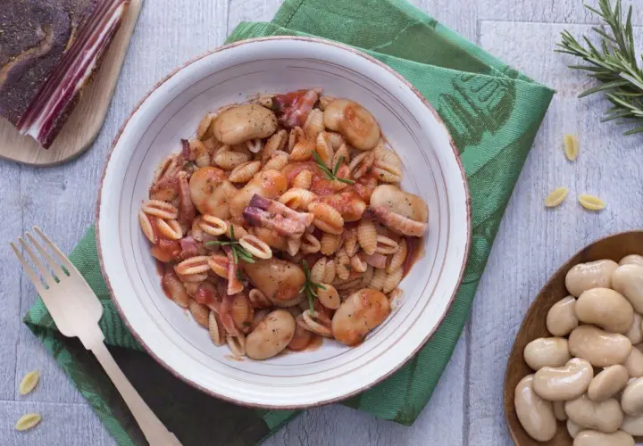 Gnocchetti alla sarda con fagioloni, pancetta y salsa de tomate, decorado con romero.