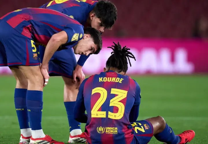 Piłkarze FC Barcelona zmartwieni po kontuzji kolegi. Koundé siedzi na murawie, koledzy pochylają się nad nim.
