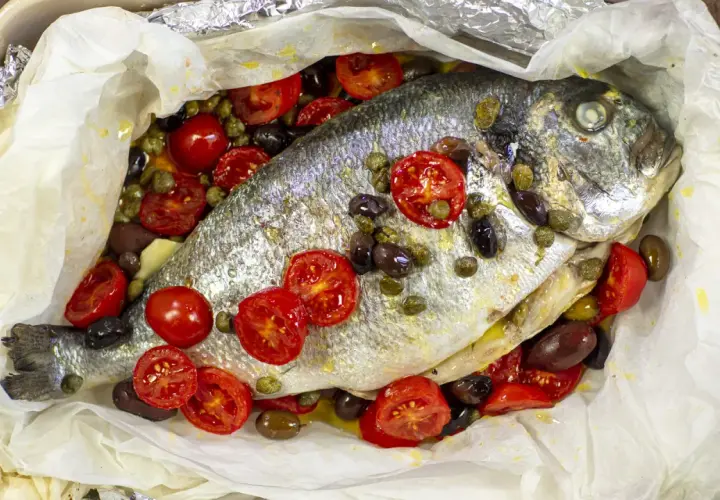 Orata al cartoccio con pomodorini, olive e capperi, un piatto profumato e saporito pronto per essere gustato.