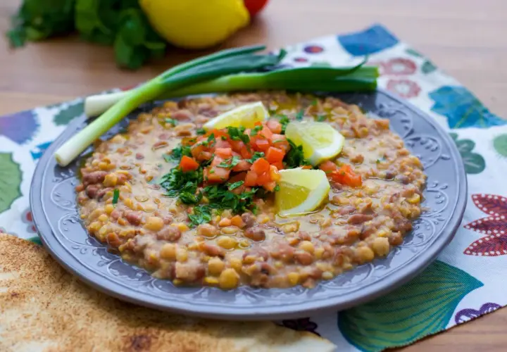 En tallrik med en mustig foul-rätt, toppad med tomat, persilja och citron. Ett utsökt recept för en smakrik måltid.