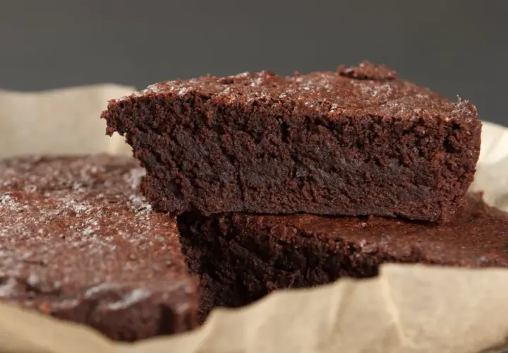 Wilgotne brownie bez jajek, posypane cukrem pudrem, ułożone na papierze do pieczenia.