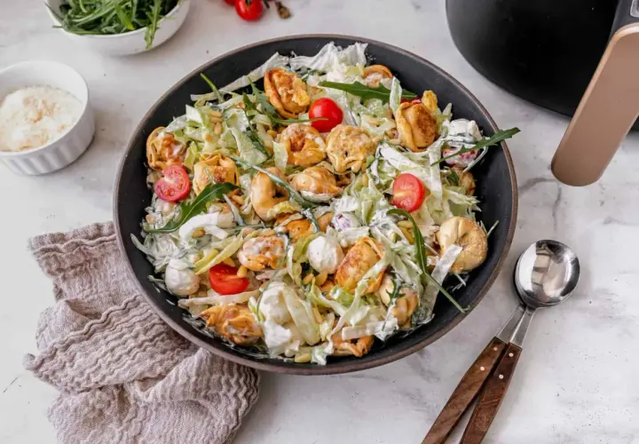 Ein üppiger italienischer Salat mit Tortellini, Kirschtomaten, Rucola und Pinienkernen, übergossen mit einer cremigen Sauce.