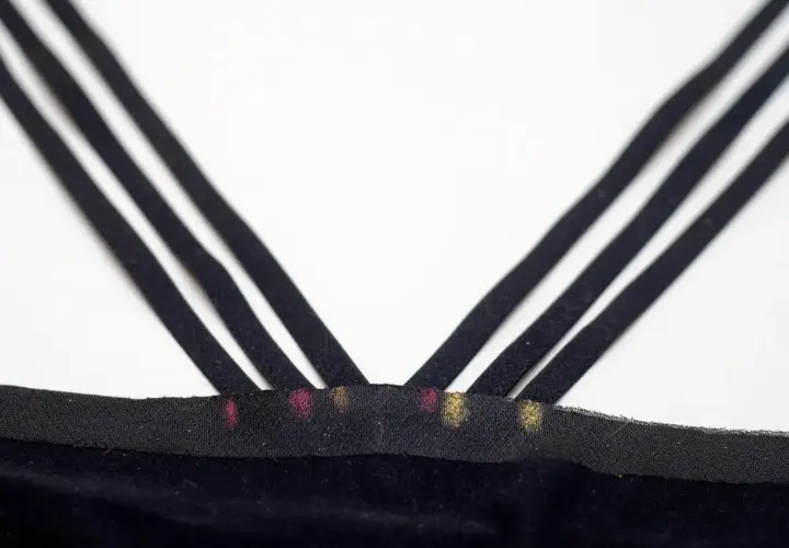 Close-up of three black bra straps crisscrossing over a black fabric band with pink and gold marks.