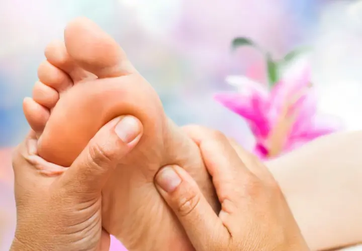 Close-up of hands massaging a foot with a blurred pink flower in the background.