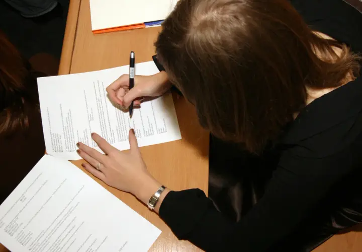 Kobieta pisze na kartce, ucząc się, jak zostać rzeczoznawcą majątkowym.