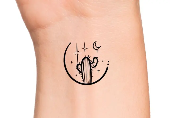 Minimalistyczny kaktus tatuaz na nadgarstku, otoczony księżycem i gwiazdami.