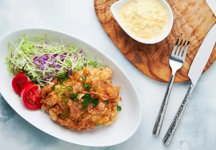 Crispy nanban food, a delicious fried chicken dish, served with shredded cabbage, tomato slices, and a creamy tartar sauce.