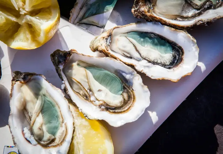 Trois huîtres vertes fraîchement ouvertes, prêtes à être dégustées avec des quartiers de citron.