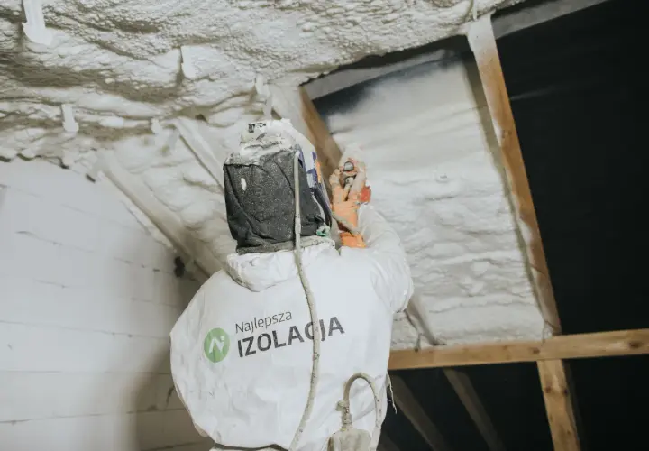 Pracownik w kombinezonie natryskuje twardą piankę poliuretanową na poddasze, tworząc skuteczną izolację.