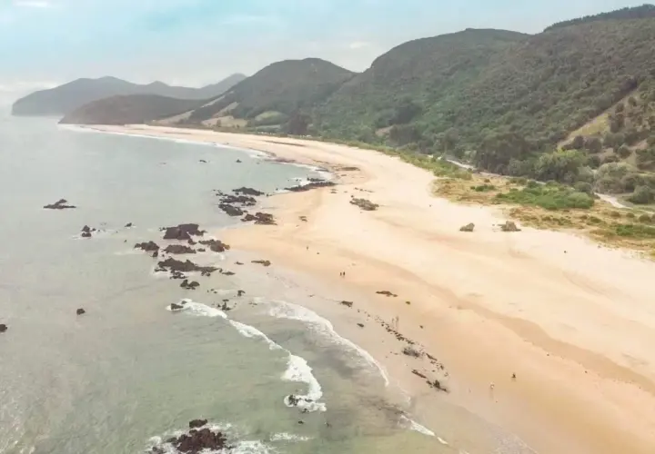 Vista aérea de la **playa Trengandin**, con arena dorada, rocas oscuras y colinas verdes al fondo.
