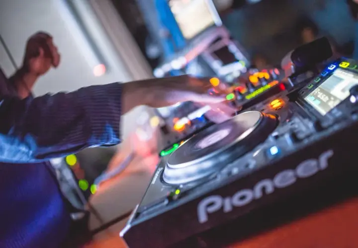 Les mains d'un DJ mixent sur une platine Pioneer, là où les DJs trouvent leur musique. Lumières colorées et ambiance festive.