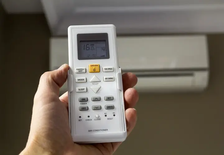 Mano sujetando control remoto de aire acondicionado, mostrando 16°C. La "A" en el aire acondicionado podría indicar modo automático o alguna función específica.