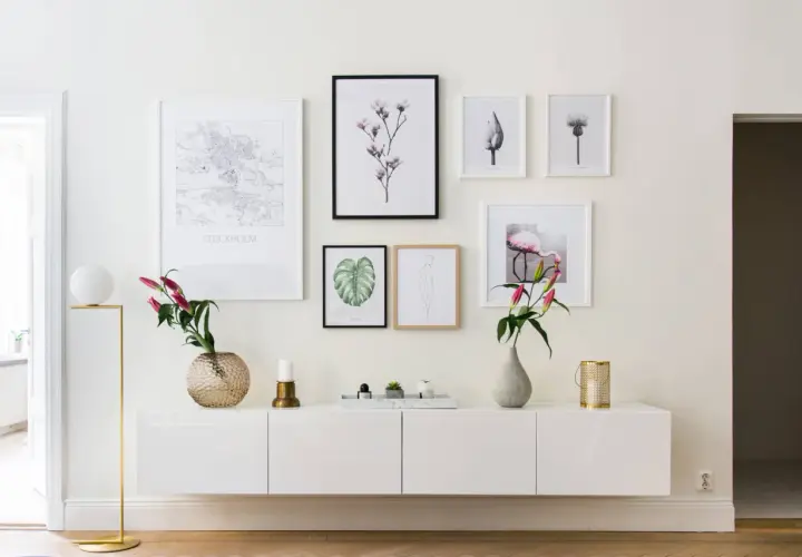 Ett modernt, vitt sideboard med konstverk ovanför, inklusive en Stockholmskarta och en flamingo. En golvlampa och vaser ger en stilfull touch.
