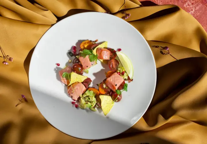 Talerz z łososiem, awokado, pomidorkami i nachos na złotym tle.