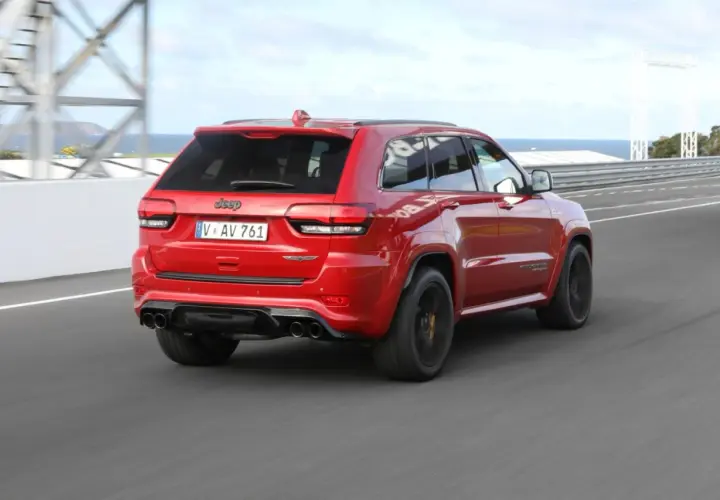 Czerwony Jeep Grand Cherokee Trackhawk SRT pędzi po torze wyścigowym, jego potężny silnik brzmi jak burza.