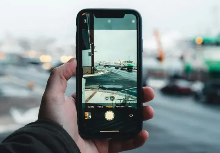Dłoń trzyma smartfon, na ekranie którego widać zimowy krajobraz portu. Zbliżenie uchwyciło subtelny pixel shift, dodając głębi scenie.
