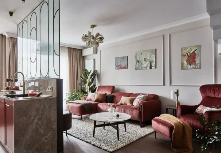 Elegancki salon z bordową kanapą i fotelem. Modne ściany w salonie zdobią obrazy, a kuchnia oddzielona jest ażurową ścianką.