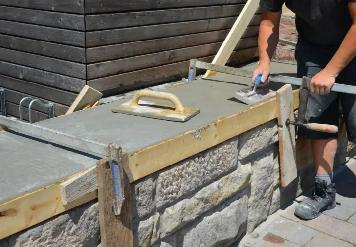 Arbeiter glättet frischen Beton auf einer **Wandschalung**. Der Aufbau der Schalung aus Holz und Metall ist gut sichtbar.