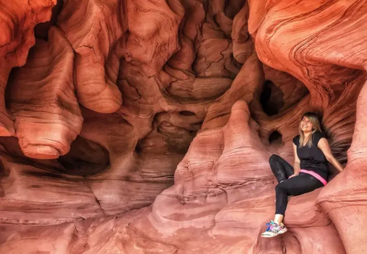 Una mujer sonríe sentada en las impresionantes formaciones rocosas de las coves de Can Riera, un paisaje natural de arenisca erosionada.
