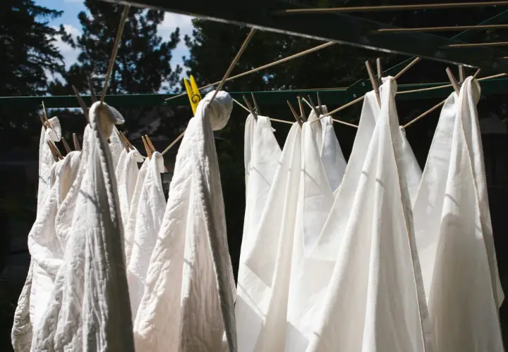 Des linges blancs, dont un pantalon, sèchent au soleil. Une astuce pour savoir comment blanchir un pantalon blanc : le laisser sécher à l'air libre après un bon lavage.